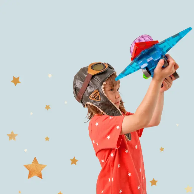 Ένα μικρό αγόρι με κράνος κρατάει χαρούμενα ένα παιχνίδι αεροπλάνο φτιαγμένο με MAGNA-TILES.